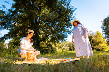 Caucasian mother with her young daughter sitting on a blanket in a bright park enjoying a family picnic and leisure activities in warm summer weather. Low angle view