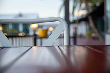 Wooden table and white metal chair in an outdoor cafe at sunset with soft natural lighting and blurred background. Cozy and minimalist atmosphere ideal for coffee shop, or lifestyle concepts.