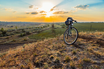 Naklejka premium A bicycle stands on a hill against the backdrop of the sunset sky, with a valley and a field of sunflowers in the background.