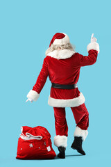 Santa Claus with bag full of gifts on blue background, back view