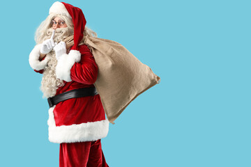 Santa Claus with bag full of gifts showing silence gesture on blue background