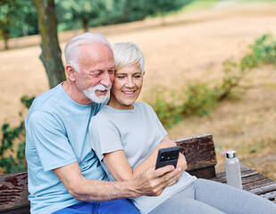 Happy active senior couple having fun using smartphone and wearing sportswear, checking music or an exercise app, after having an exercise sport activity outdoors