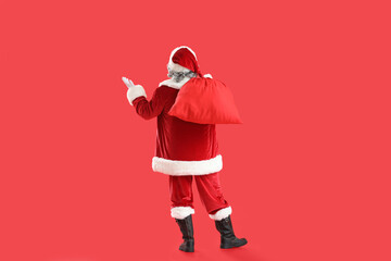 Santa Claus with bag full of gifts on red background, back view