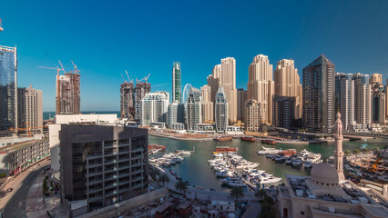 Naklejka premium Yachts in Dubai Marina flanked by the Al Rahim Mosque and residential towers and skyscrapers aerial timelapse.