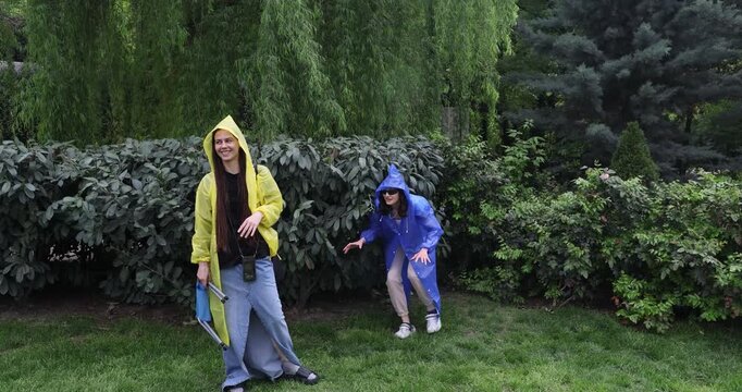 Woman steps out from bushes jumping toward girl friend with shout. Female prankster waves arms and giggles chasing partner few steps for fun
