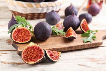 Cutting board with fresh ripe figs and arugula leaves on white wooden background, closeup