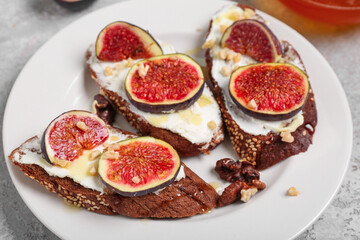 Plate of sandwiches with fresh ripe fig on grey grunge background, closeup
