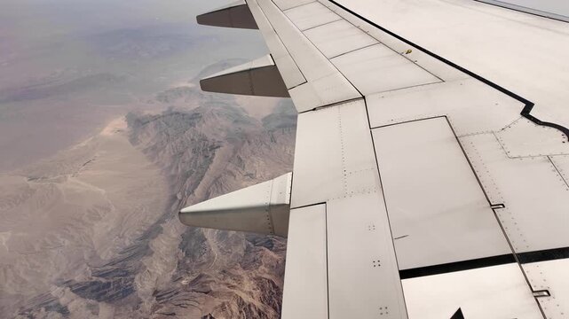 Airplane flying above rocky mountains, side window view