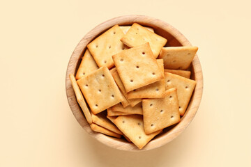 Wooden bowl with tasty crackers on beige background, closeup
