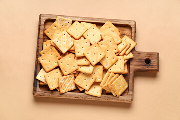 Wooden board with tasty crackers on beige background, closeup