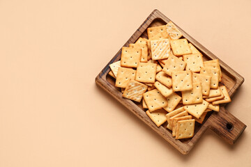Wooden board with tasty crackers on beige background