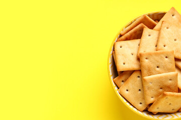 Bowl with tasty crackers on yellow background, closeup
