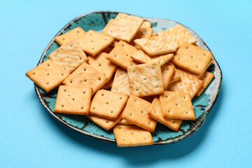 Plate with tasty crackers on blue background, closeup
