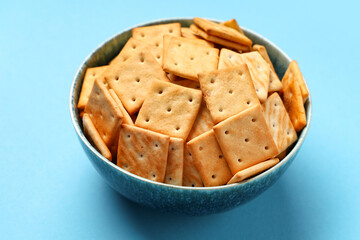 Bowl with tasty crackers on blue background, closeup