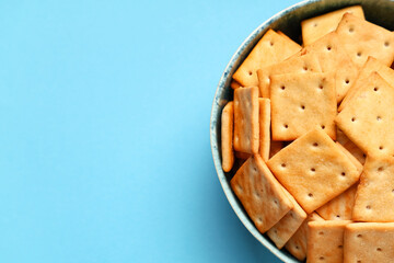 Bowl with tasty crackers on blue background, closeup