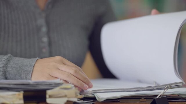 Close-up of woman flipping through printed financial documents with charts and data. Budget review and report creation theme.