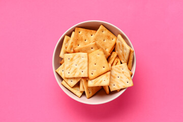 Bowl with tasty crackers on pink background, closeup