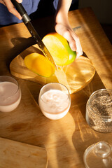 Hands slicing ripe mango with chia seeds and yogurt drinks nearby