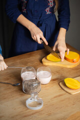 Child sprinkling chia seeds while girl slices fresh mango for dessert