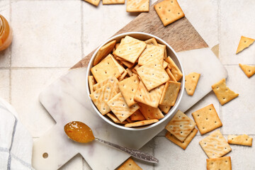 Composition with bowl of tasty crackers and teaspoon with honey on beige tile background, closeup