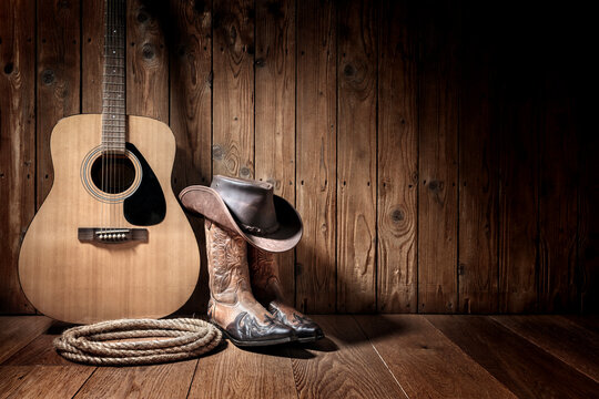 Cowboy hat, boots and acoustic guitar, against blank wooden plank panel grunge background with copy space