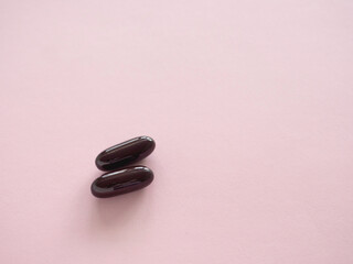 Two dark brown pills against a light pink background. Close up with copy space. Health supplement concept.