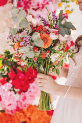 Beautiful bride holding a vibrant bouquet of colorful flowers during a joyful wedding ceremony in a floral decorated venue