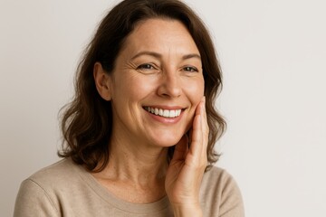 Smiling woman with healthy teeth and glowing skin, gently touching her face in soft natural light.