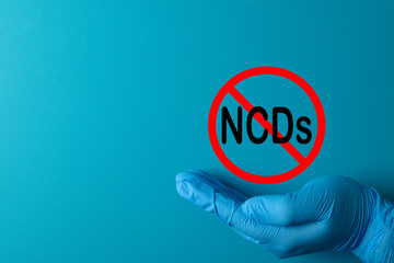 Prevention of NCDs (Non-Communicable Diseases) concept. A doctor's hand holds a stop sign over the acronym for chronic diseases like cancer, diabetes, stroke, and heart disease awareness.