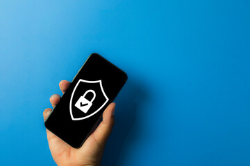 Mobile cybersecurity and data protection concept. A hand holds a smartphone showing a security shield with a padlock, symbolizing antivirus software, privacy, and protection from hacking threats.