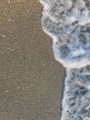 Waves gently wash over a sandy beach, leaving a trail of foam in the early morning light