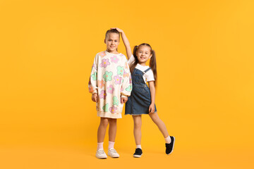 Little girls comparing their heights on orange background