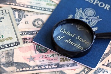 US passport and magnifying glass on the background of many dollar bills