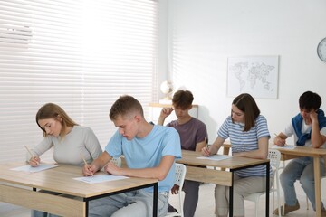 Students taking exam at wooden table indoors