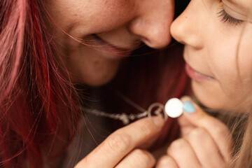 Mother and daughter holding silver pendants with blue gemstones, symbolizing love and connection....