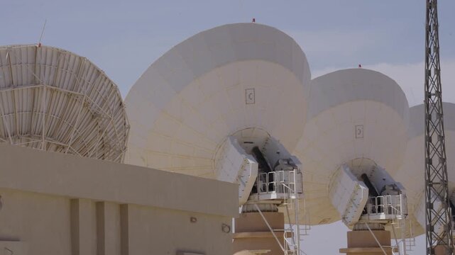 A static shot showcasing multiple generations of satellite technology. A large, complex mesh dish stands beside modern, solid parabolic antennas at a ground station.