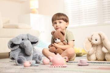 Cute little boy playing tea party with his toys indoors