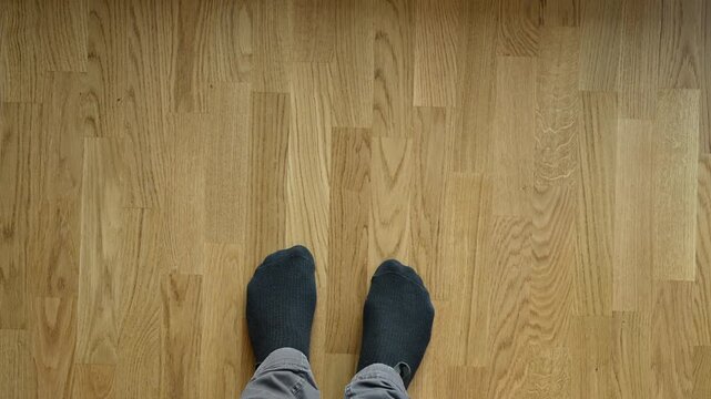 Top view of male feet in black socks standing on oak wood parquet floor. 4K