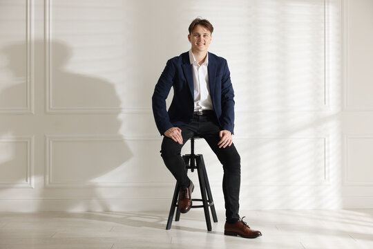 Man in stylish jeans on stool near white wall indoors