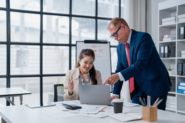 Fototapeta premium Business executive mentoring young female employee, pointing at laptop screen while discussing charts and working together on a project in a modern office workplace