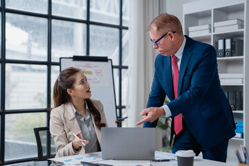 Mature male boss pointing hand at laptop screen discussing project with young asian female...