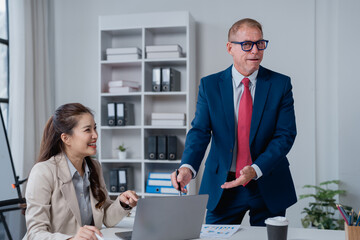 Diverse business colleagues brainstorming ideas and discussing work, analyzing data on a laptop and documents during a meeting in a contemporary corporate office environment
