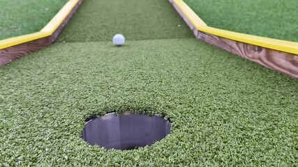 Close-up slow motion of a golf ball rolling on the green and falling into the hole. Perfect putt, success and precision in professional golf game. - Powered by Adobe