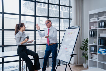 Fototapeta premium Business professionals collaborating and discussing a business plan during an informal office meeting, with one executive explaining ideas on a whiteboard