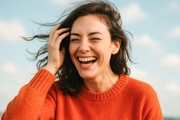 Candid close-up of happy woman in orange sweater laughing in the breeze against soft sky, authentic emotion and positivity — generative AI
