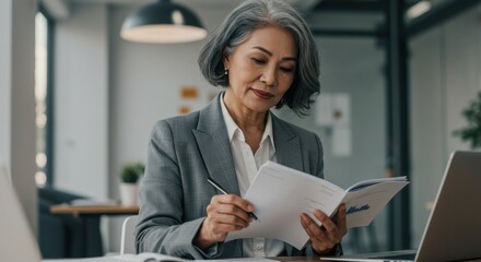 Mature asian businesswoman reviewing documents at her desk in a modern office space