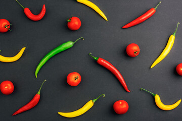 Colorful chili peppers and fresh tomatoes arranged on dark background, top view. Spicy food and healthy eating concept. Pattern, flat lay