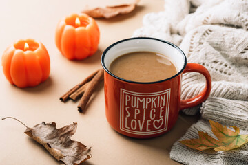 Coffee pumpkin latte in orange cup, candles and knitted sweater. Autumn still life, Halloween or Thanksgiving concept. Closeup