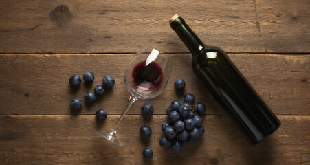 A bottle, wine in a glass and fresh grapes lie on a wooden table top view