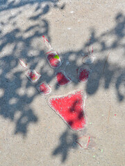 A textured concrete surface features a prehistoric dinosaur footprint impression filled with red color. The footprint consists of a three-toed design indicative of theropod dinosaurs.